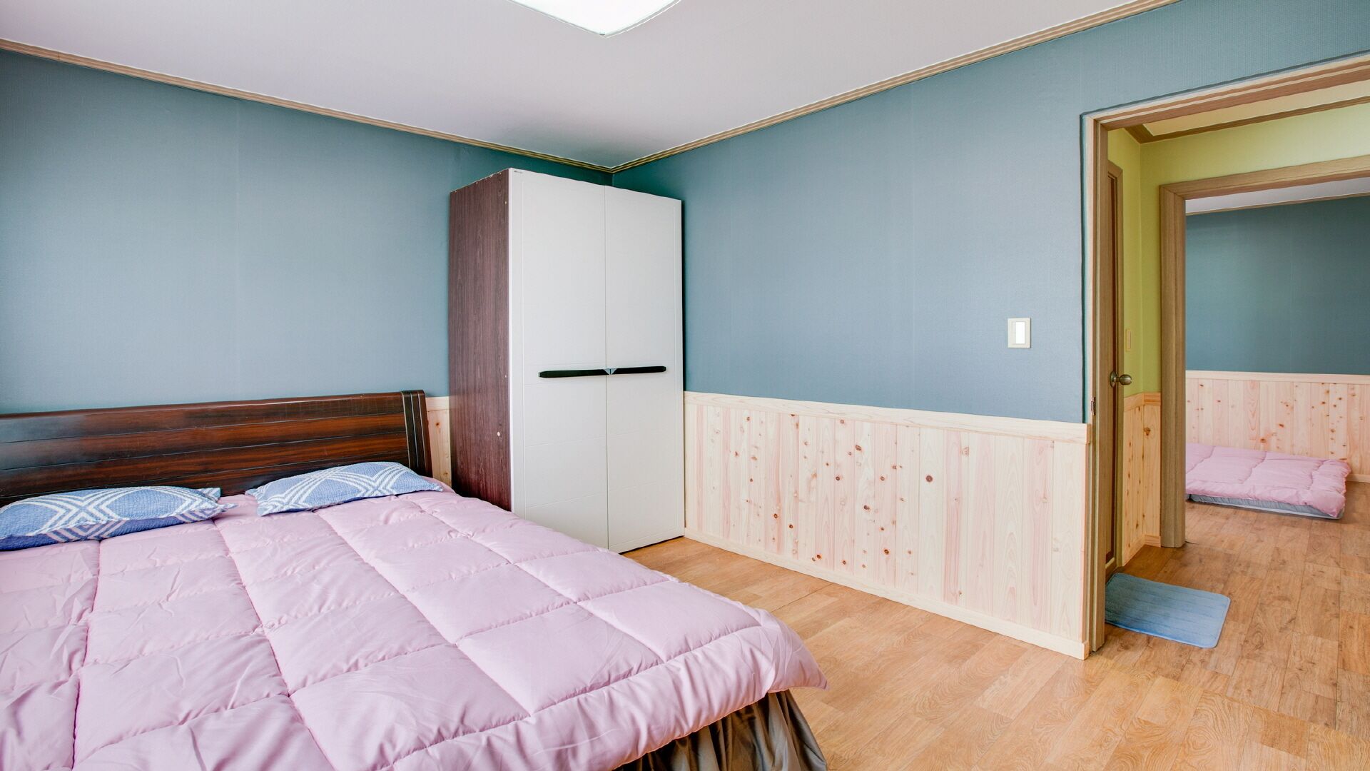 A bedroom with a bed, a wardrobe, and a door leading to another room.