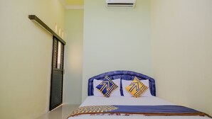 A single bed with a headboard, two pillows with geometric patterns, a bedspread with a geometric design, an air conditioning unit on the wall, and a window with a closed shutter. - SPOT ON 2431 Tf Homestay (Caruban)