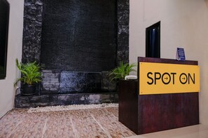 A reception area with a 'SPOT ON' sign, a black textured wall, and two potted plants. - SPOT ON 2431 Tf Homestay (Caruban)