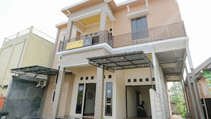 A two-story house with a balcony, a sign indicating 'SPOT ON' and 'Homestay', and a covered entrance. - SPOT ON 2431 Tf Homestay (Caruban)