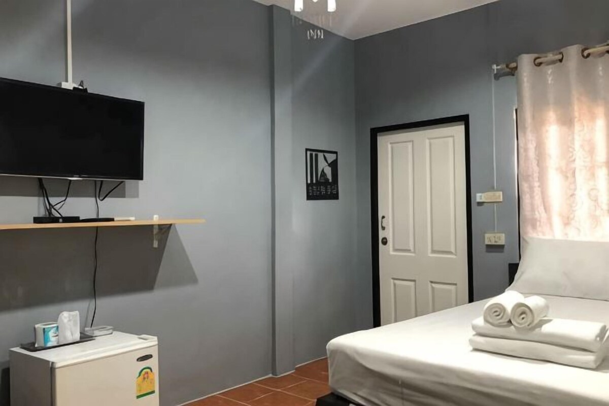 A bedroom with a bed, a TV mounted on the wall, a door, and a small cabinet.