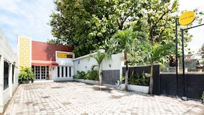 A paved entrance with a 'SPOT ON' sign, a building with a red roof, and a white wall with a geometric pattern. - SPOT ON 2419 Rumah Nugraha Hotel Syariah (Yogyakarta)