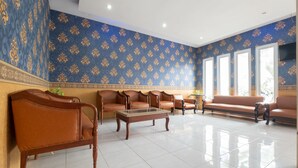 A spacious lobby with a patterned blue and gold wall, leather sofas, a glass coffee table, and large windows allowing natural light. - SPOT ON 2419 Rumah Nugraha Hotel Syariah (Yogyakarta)