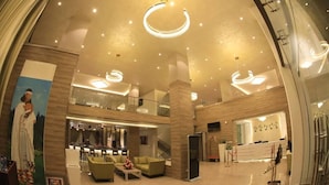Un hall d’entrée spacieux avec un plafond haut, des luminaires modernes, un comptoir de réception et un espace détente avec des canapés et une table basse.