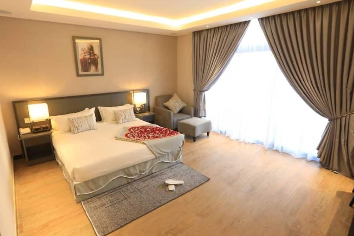 A hotel room with a large bed, bedside tables, a chair, a desk, and a window with curtains.