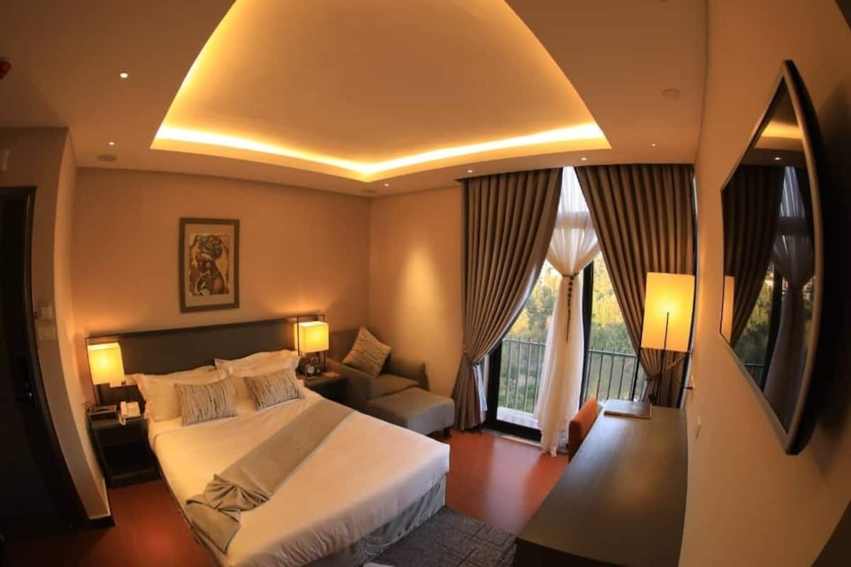 A hotel room with a large bed, a sofa, a desk, and a balcony with curtains.