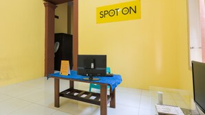 Ein Zimmer mit gelber Wand, einem 'SPOT ON'-Schild, einem Schreibtisch mit Computer und einem Stuhl.