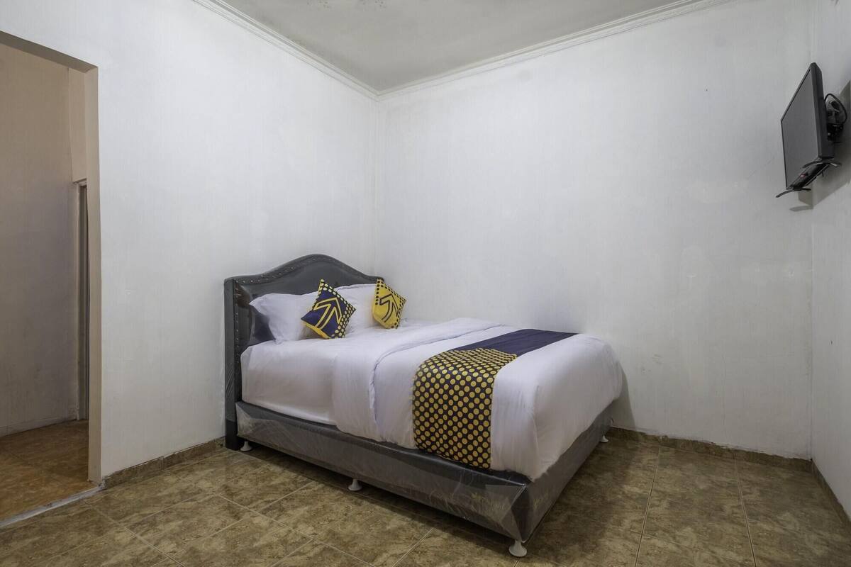 A single bed with a headboard, white walls, a tiled floor, and a television mounted on the wall.