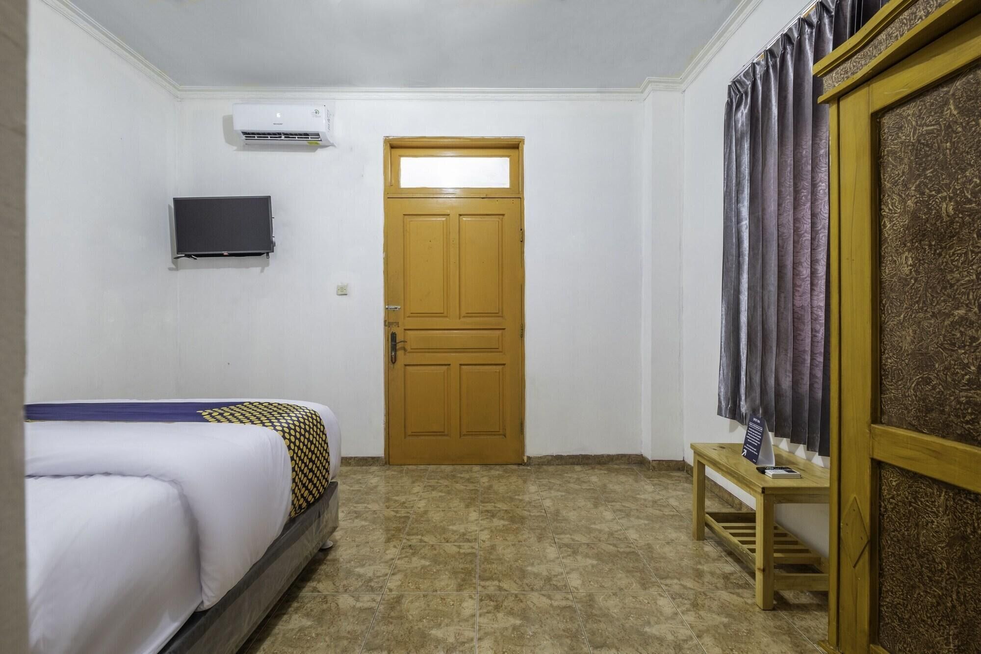 A hotel room with a bed, a television mounted on the wall, a wooden door, and a curtain.
