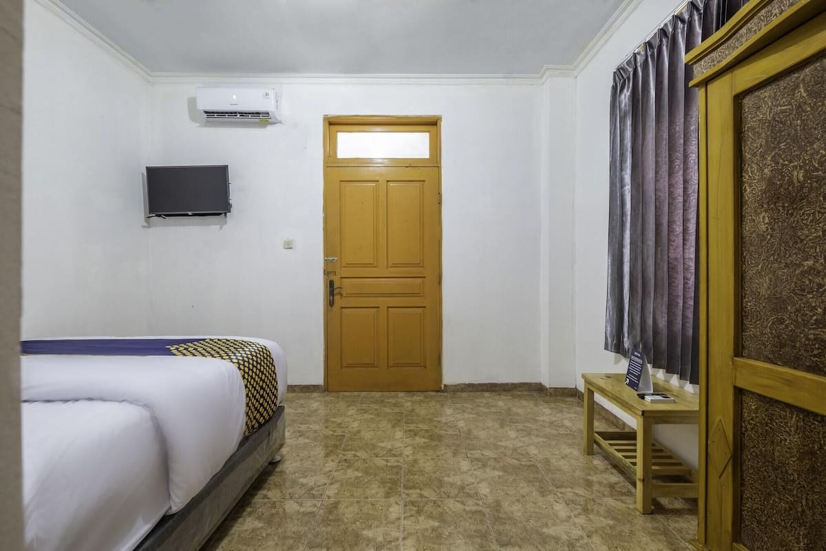 A hotel room with a bed, a television mounted on the wall, a wooden door, and a curtain.
