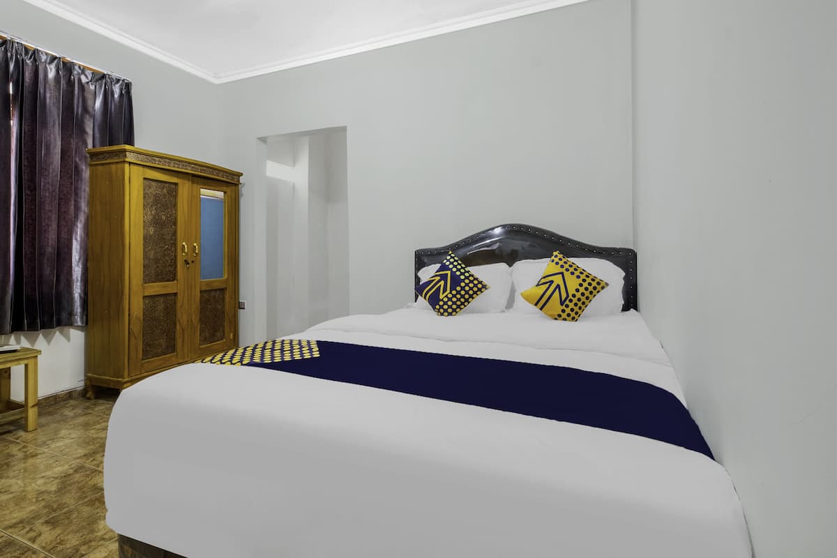A bedroom with a bed, a wooden wardrobe, and a small table.