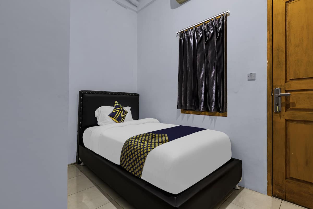 A single bed with a black headboard and white bedding, a wooden door to the right, and a curtain on the window.