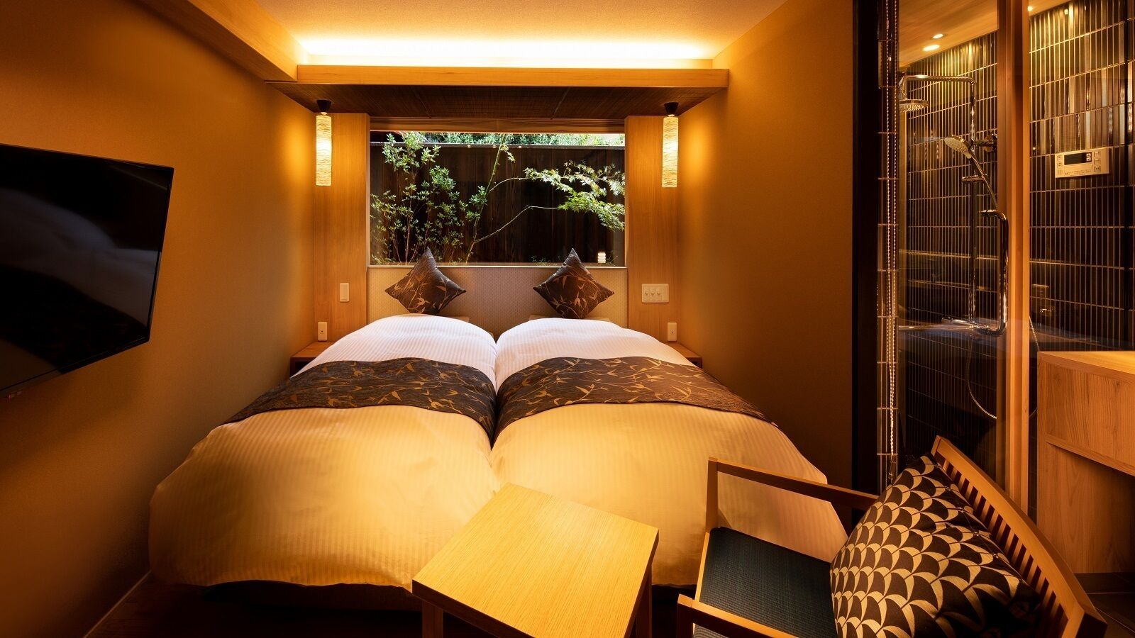 Quarto com cama, uma mesinha e janela com vista para o verde.