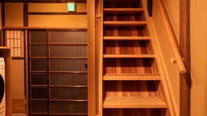 A wooden staircase with a handrail, wooden flooring, and a door with a green exit sign.