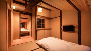 A traditional Japanese-style room with tatami flooring, a low ceiling with exposed beams, a sliding door, a small window, and a mounted television.