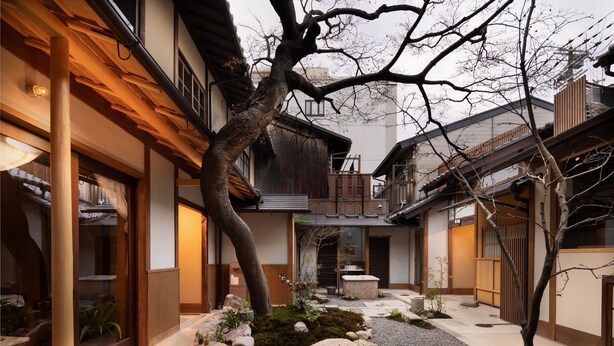 A traditional Japanese courtyard with wooden buildings, a central stone lantern, and a tree.