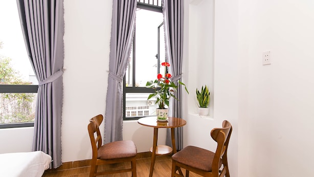 A small room with two wooden chairs, a round table, a potted plant, and a window with curtains. - SPOT ON 806 Net Viet Homestay (Da Nang)