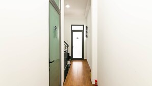 A narrow hallway with a wooden floor, a green door on the left, and a white door at the end. - SPOT ON 806 Net Viet Homestay (Da Nang)