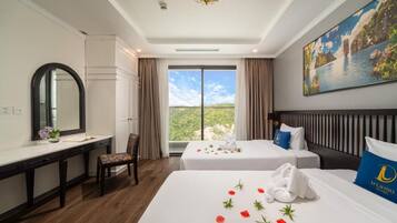 Habitación de hotel con dos camas, un escritorio, una silla, un ventanal con vistas y un cuadro en la pared.