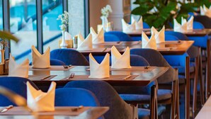 A restaurant with blue chairs, white napkins, and black pendant lights.