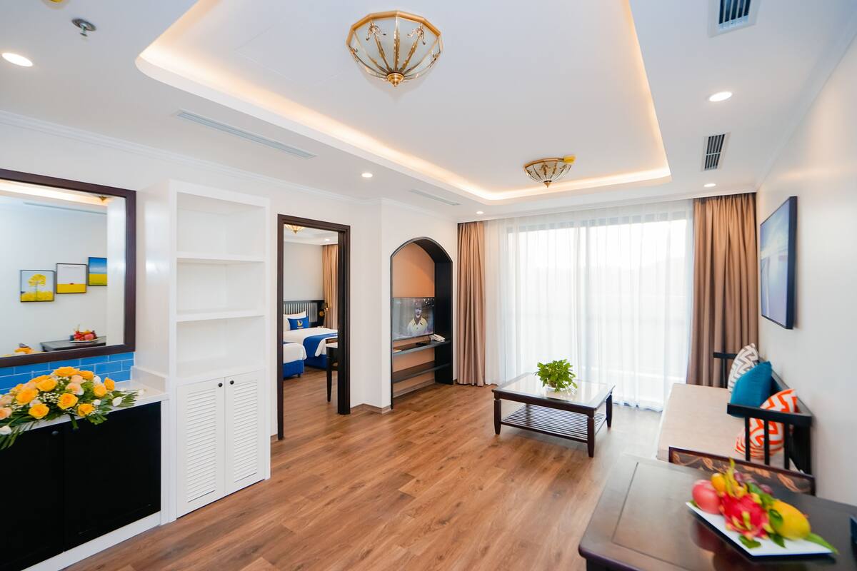 Une chambre d’hôtel moderne avec un plancher en bois, un coin repas comprenant une table et des chaises, un grand miroir et un téléviseur placé dans un coin.