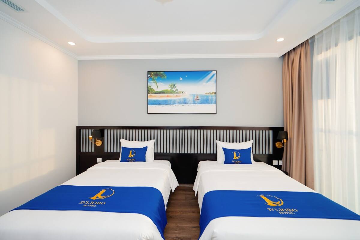Une chambre d’hôtel avec deux lits, un tableau représentant une scène de plage et une vue sur la mer.