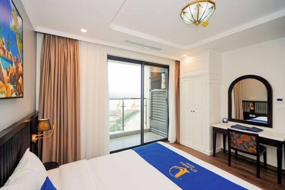 Une chambre d’hôtel avec un lit, un bureau, une chaise, une grande fenêtre et un balcon.