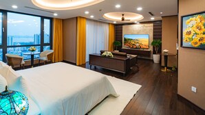 A modern hotel room with a large bed, a seating area, a TV, and a city view.