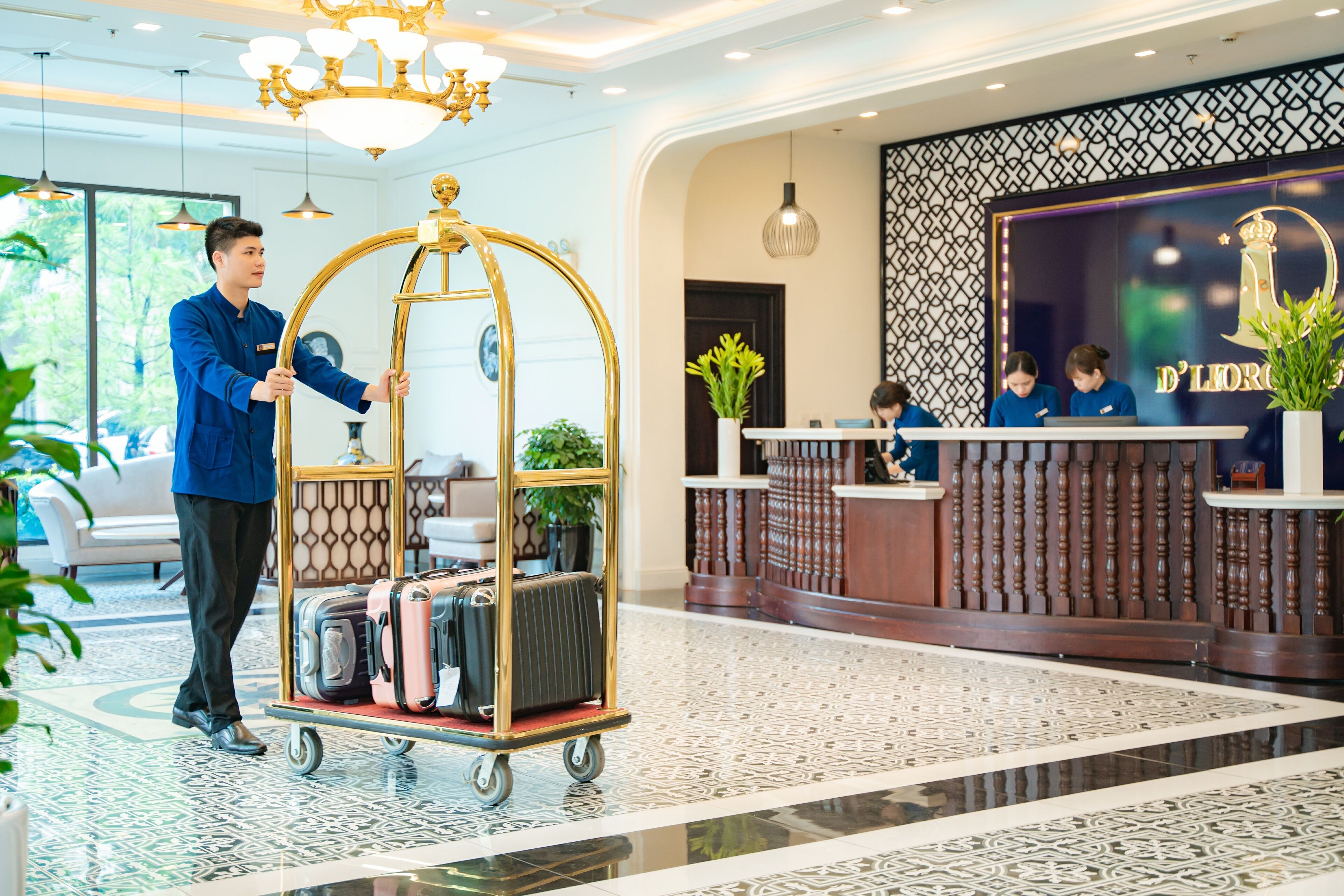 A hotel reception area with a cart of luggage, a reception desk, and a decorative wall.