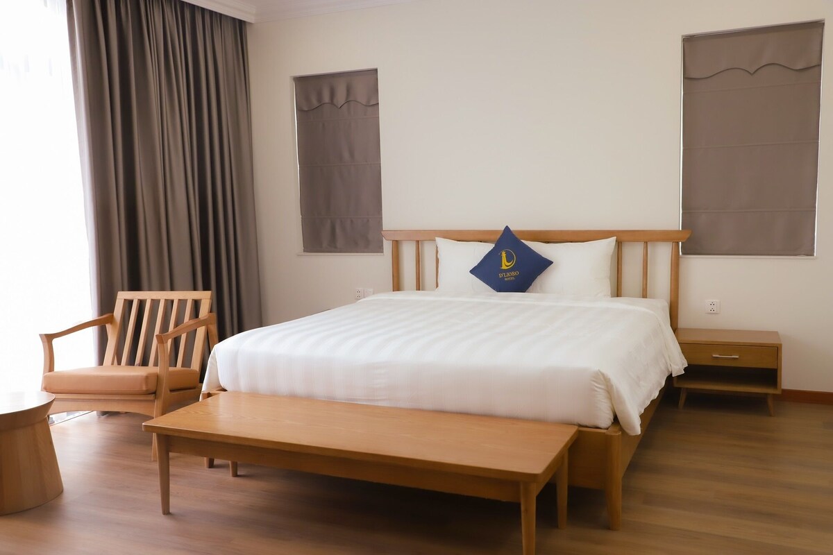 Habitación de hotel ordenada con una cama de madera, un banco, una silla y una mesita de noche.