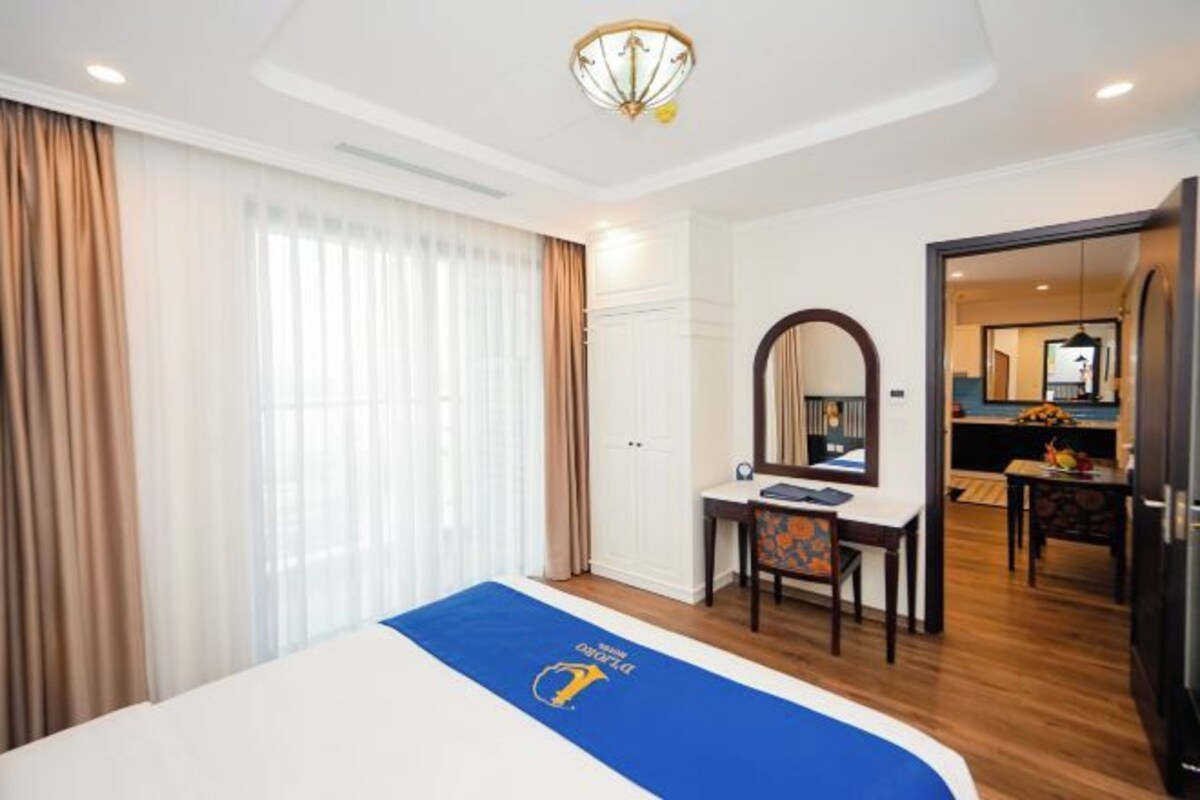 A hotel room with a bed, a desk with a chair, a mirror, and a door leading to a bathroom.