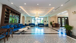 A spacious lobby with a patterned floor, blue sofas, wooden furniture, and a chandelier.