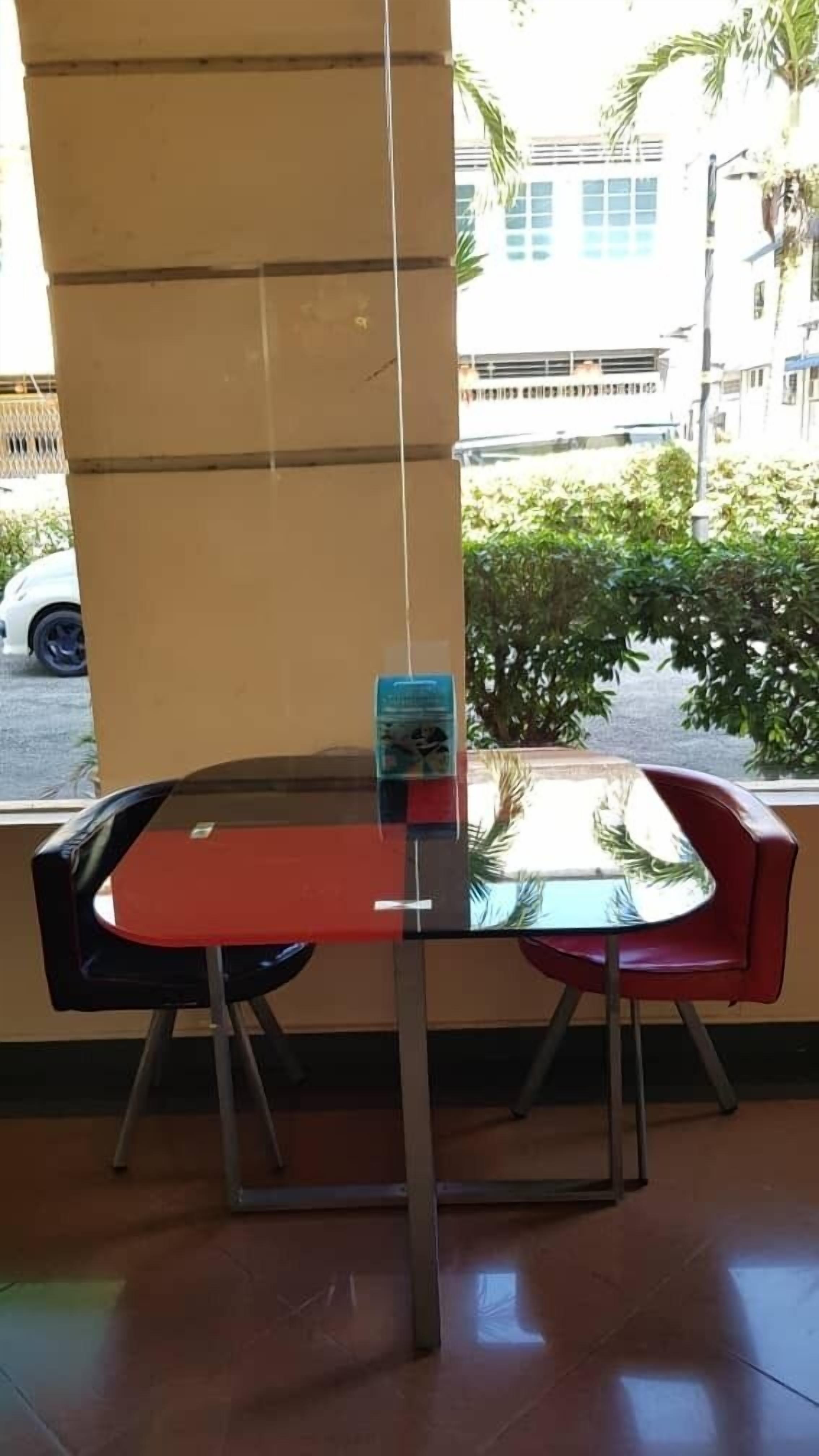 Una mesa con cubierta de vidrio, dos sillas, un letrero azul y vistas a una calle con edificios y vegetación.