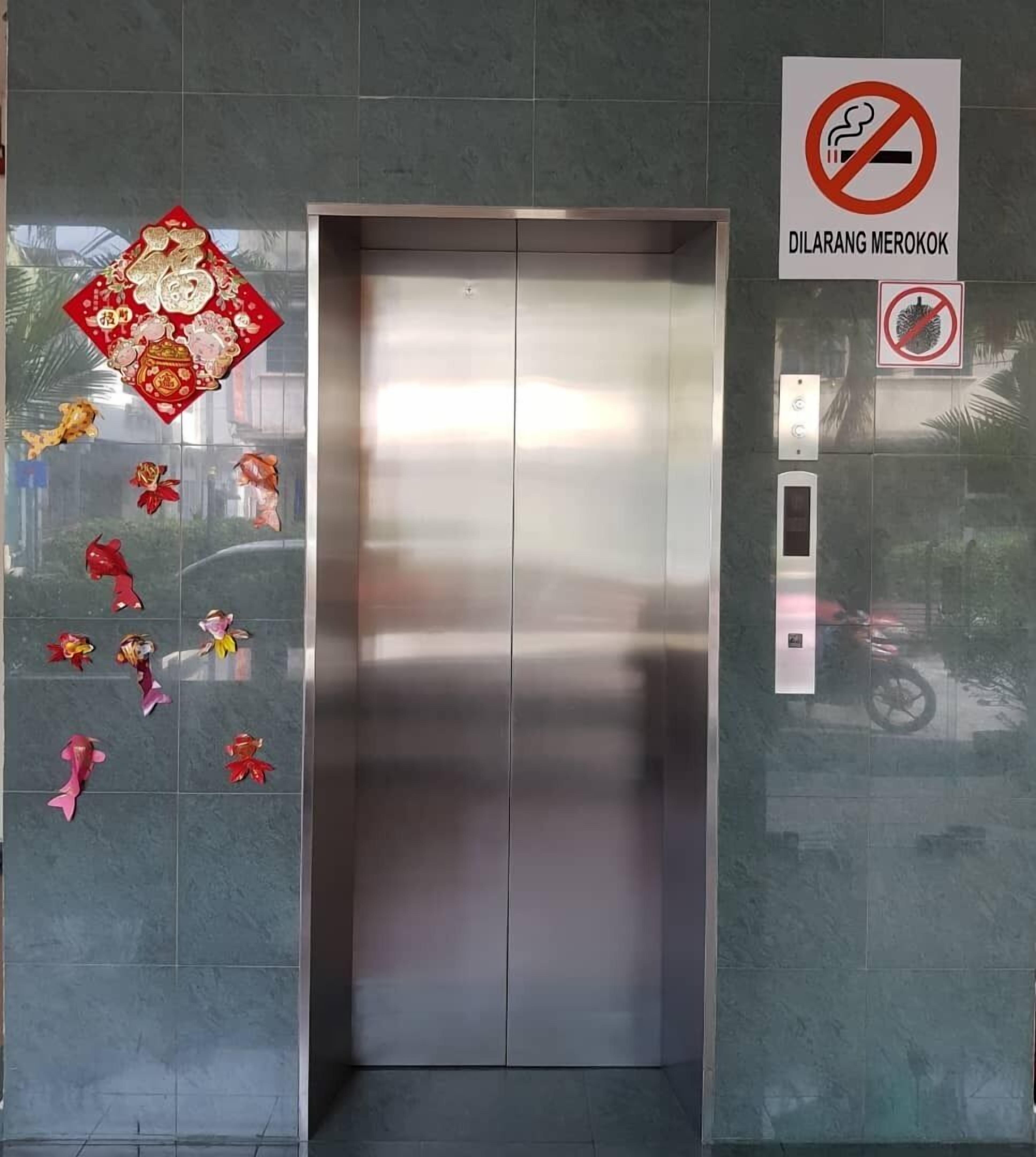 An elevator with a metallic finish, surrounded by grey tiles. There are no visible windows or doors.