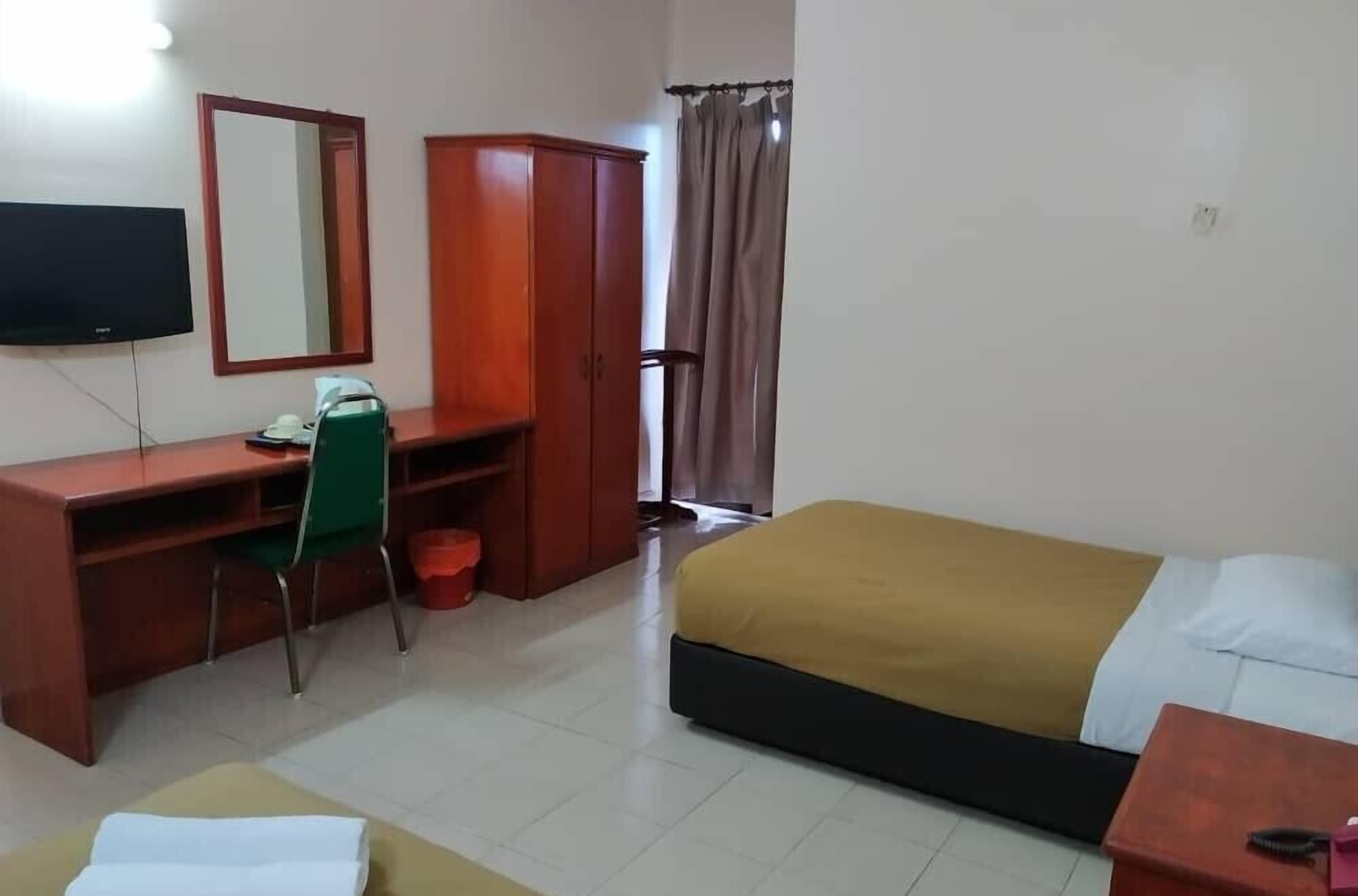 A hotel room with a bed, a desk with a chair, a wardrobe, a television, and a window with curtains.