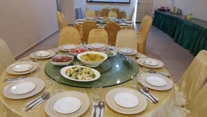 A conference room with round tables set for a meal, featuring various dishes and cutlery. - Desa Inn Hotel (Kuala Pilah)