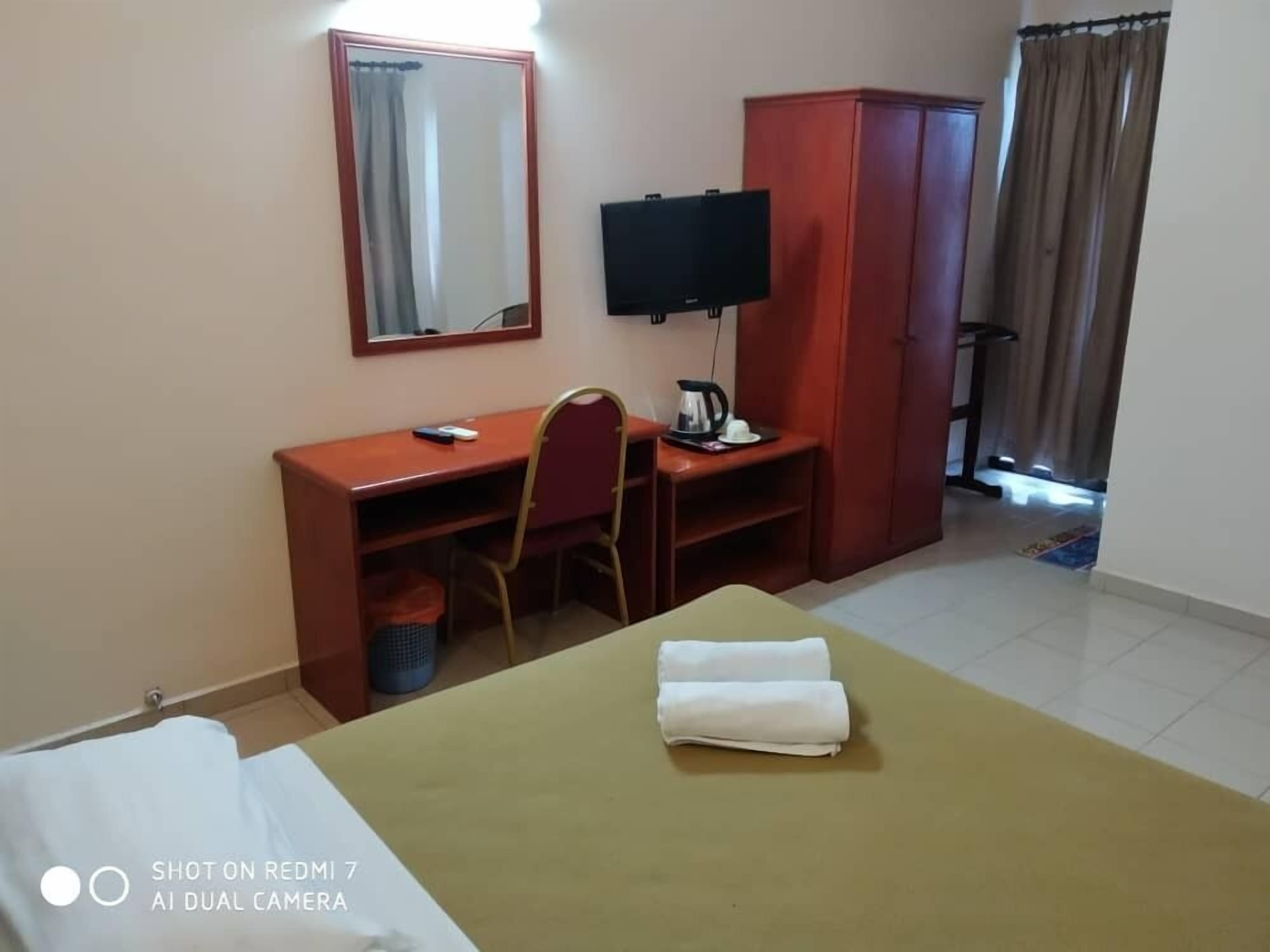 Una habitación de hotel con cama, escritorio, silla, televisor y armario.