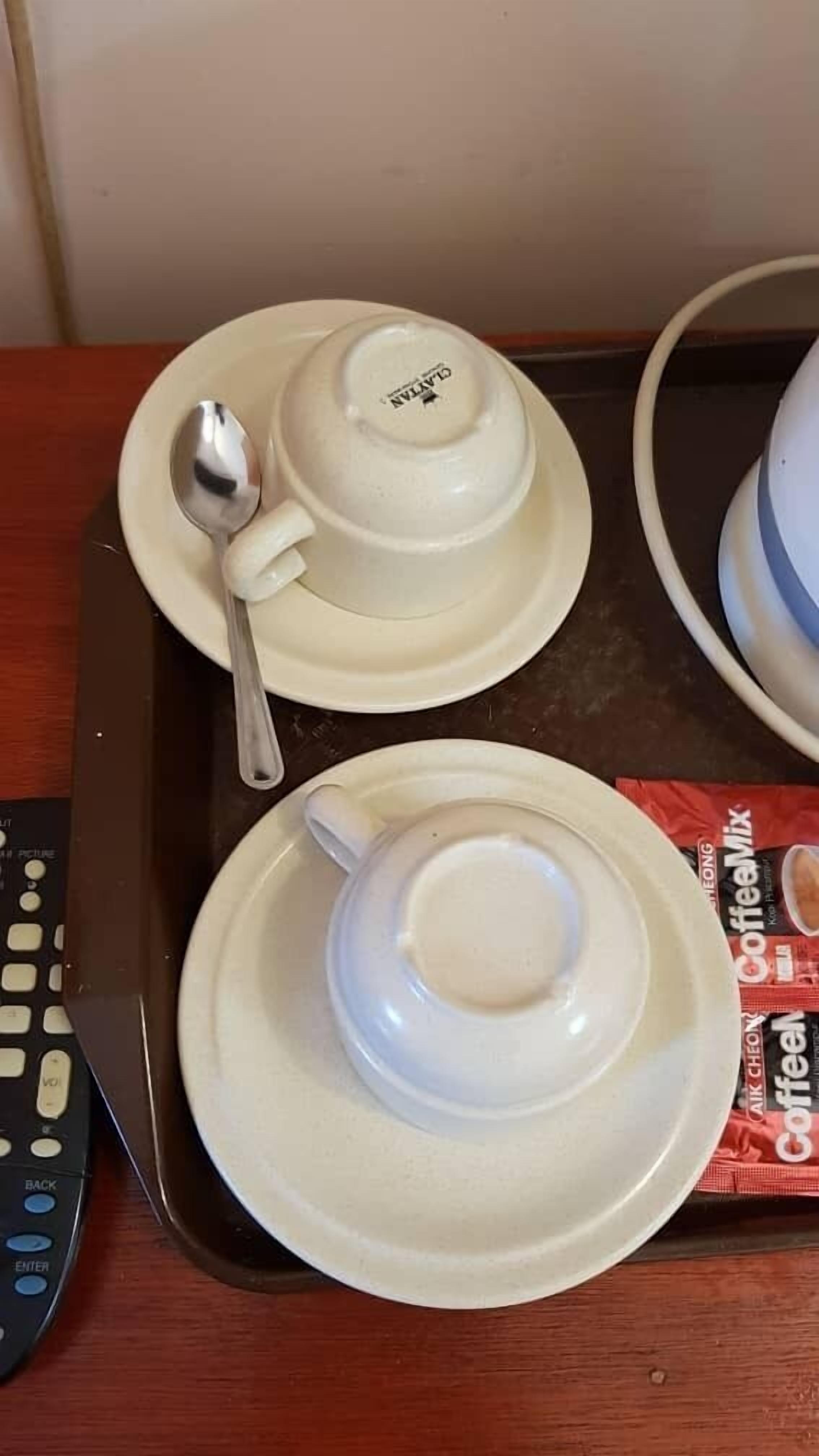 A tray with two white cups and a spoon, a remote control, and a magazine on a wooden table.
