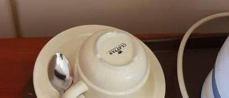 A tray with two white cups and a spoon, a remote control, and a magazine on a wooden table.