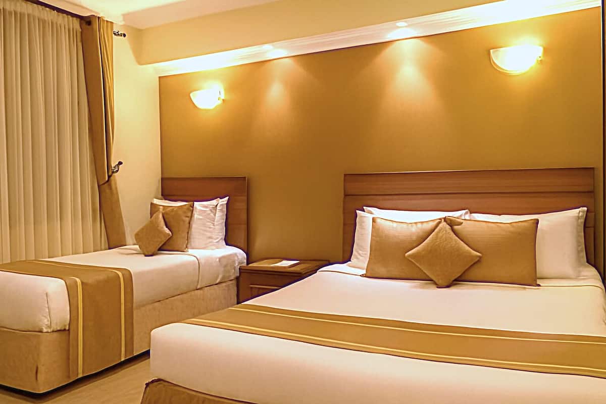 A hotel room with two beds, each with a headboard, and a nightstand between them.