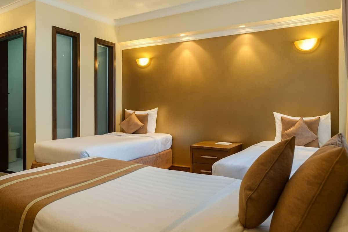 A hotel room with two single beds, a nightstand, and a bathroom visible through a glass door.