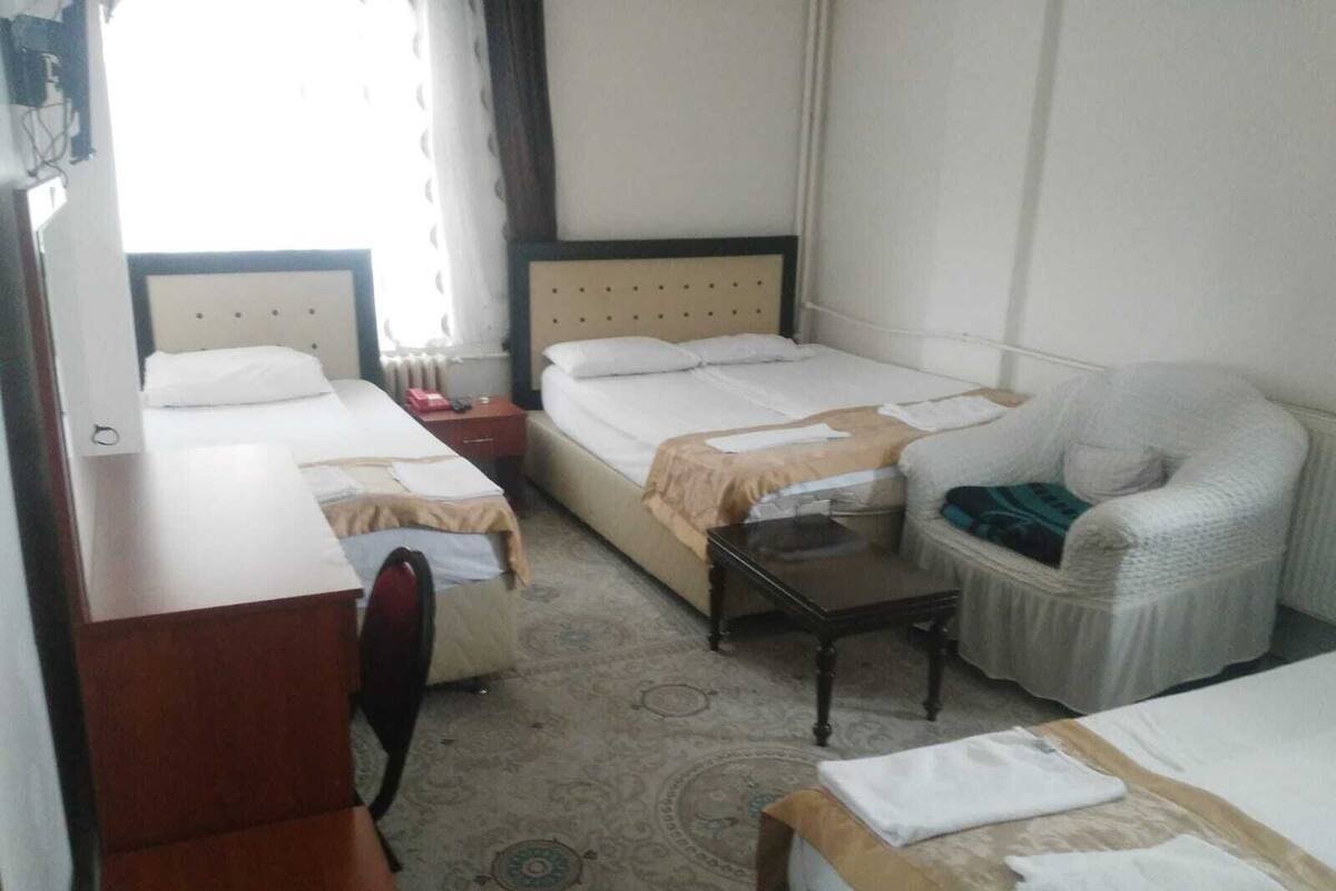 A hotel room with two single beds, a desk, a chair, a small table, and a sofa.