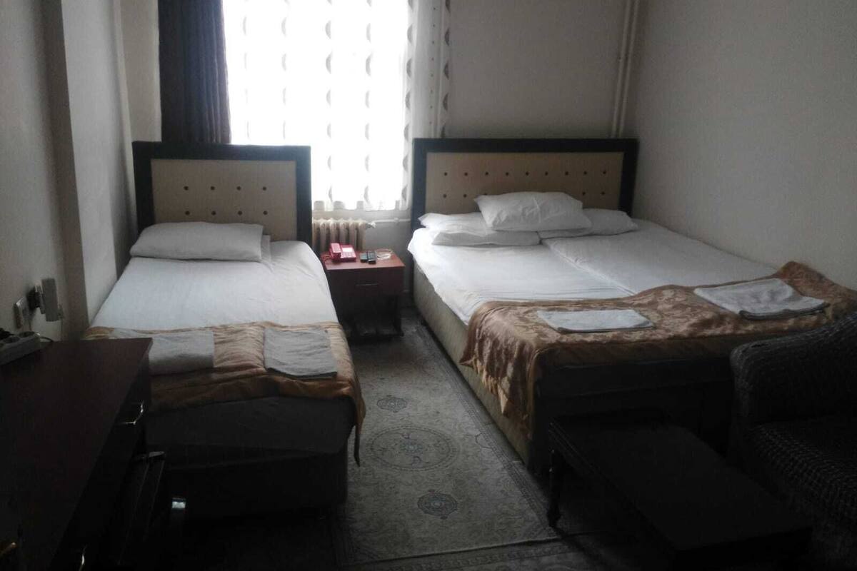 A hotel room with two single beds, a desk, a chair, and a small table with a telephone.