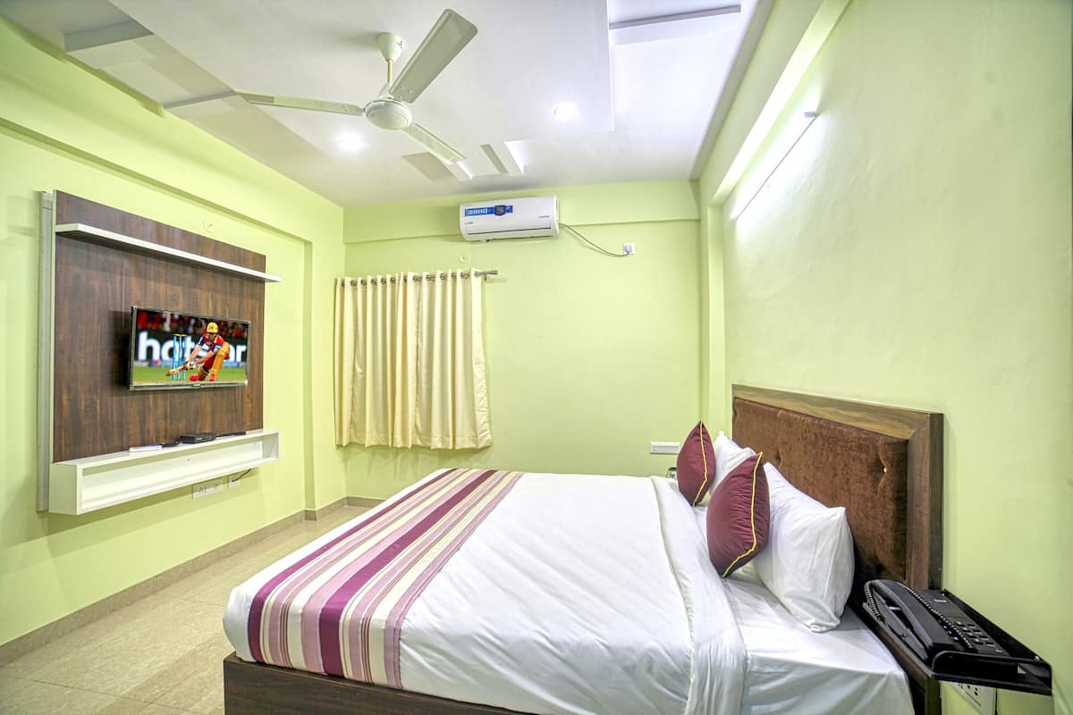 A hotel room with a bed, a television mounted on the wall, an air conditioning unit, a ceiling fan, and a window with curtains.