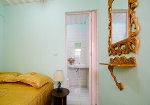 Ein Zimmer mit einem Bett, einem Nachttisch, einer Lampe, einem Spiegel und einem durchgegangenen Tür angedeuteten Badezimmer.