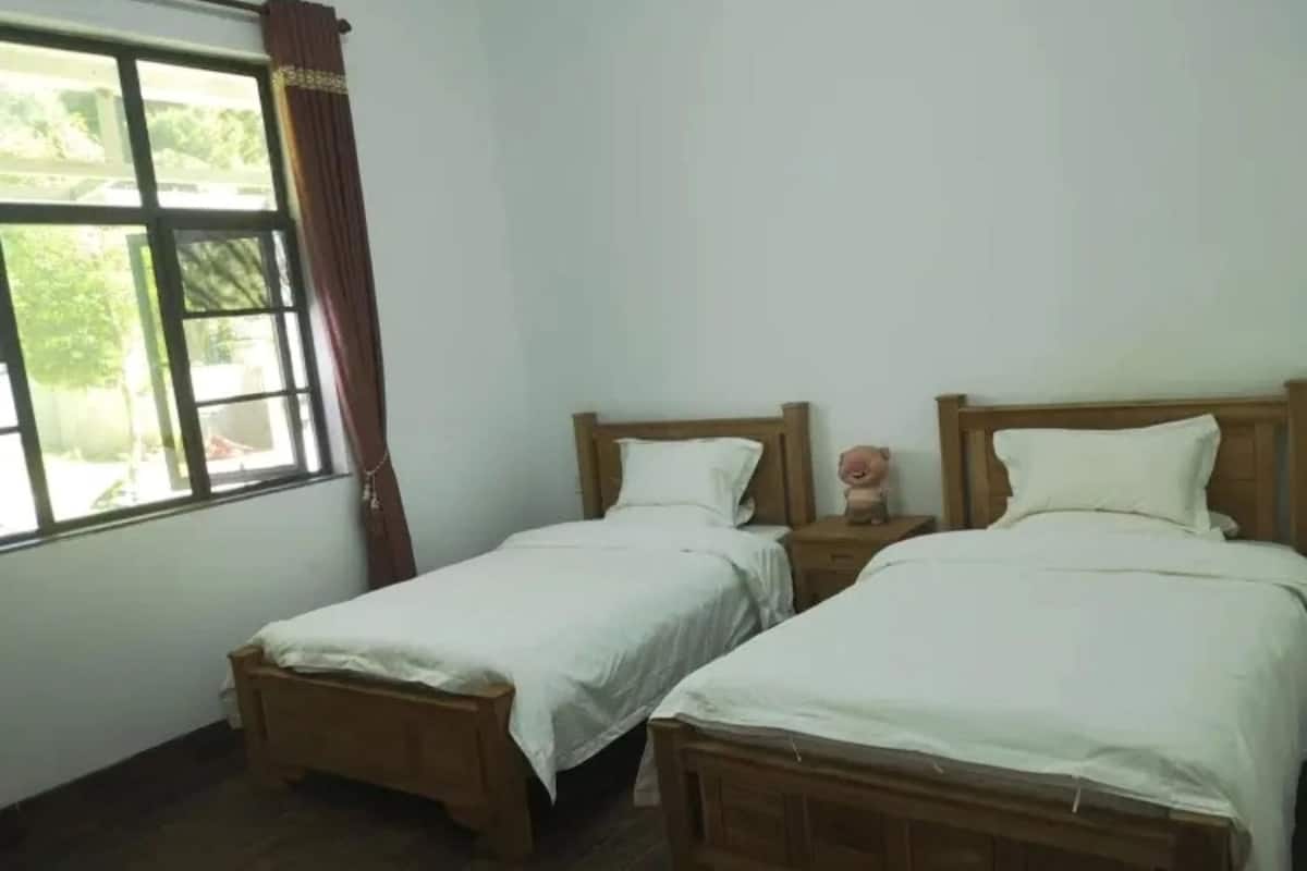 A room with two wooden beds, white bedding, a window with curtains, and a small statue on the nightstand.