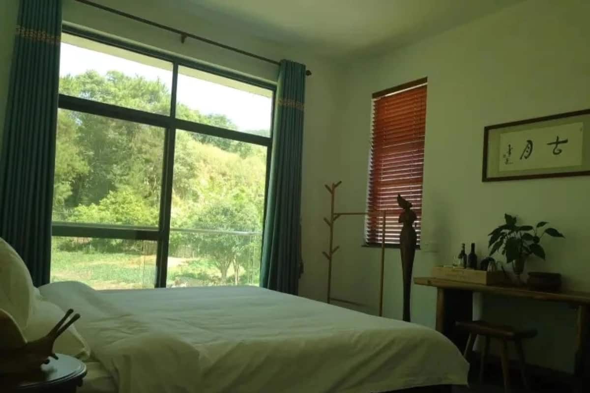A bedroom with a large window, a bed, a desk, and a chair.