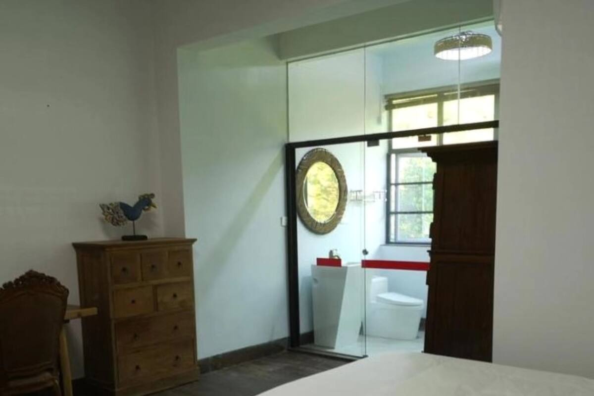 A room with two beds, a wooden dresser, a chair, a mirror, and a window with a view of the outdoors.