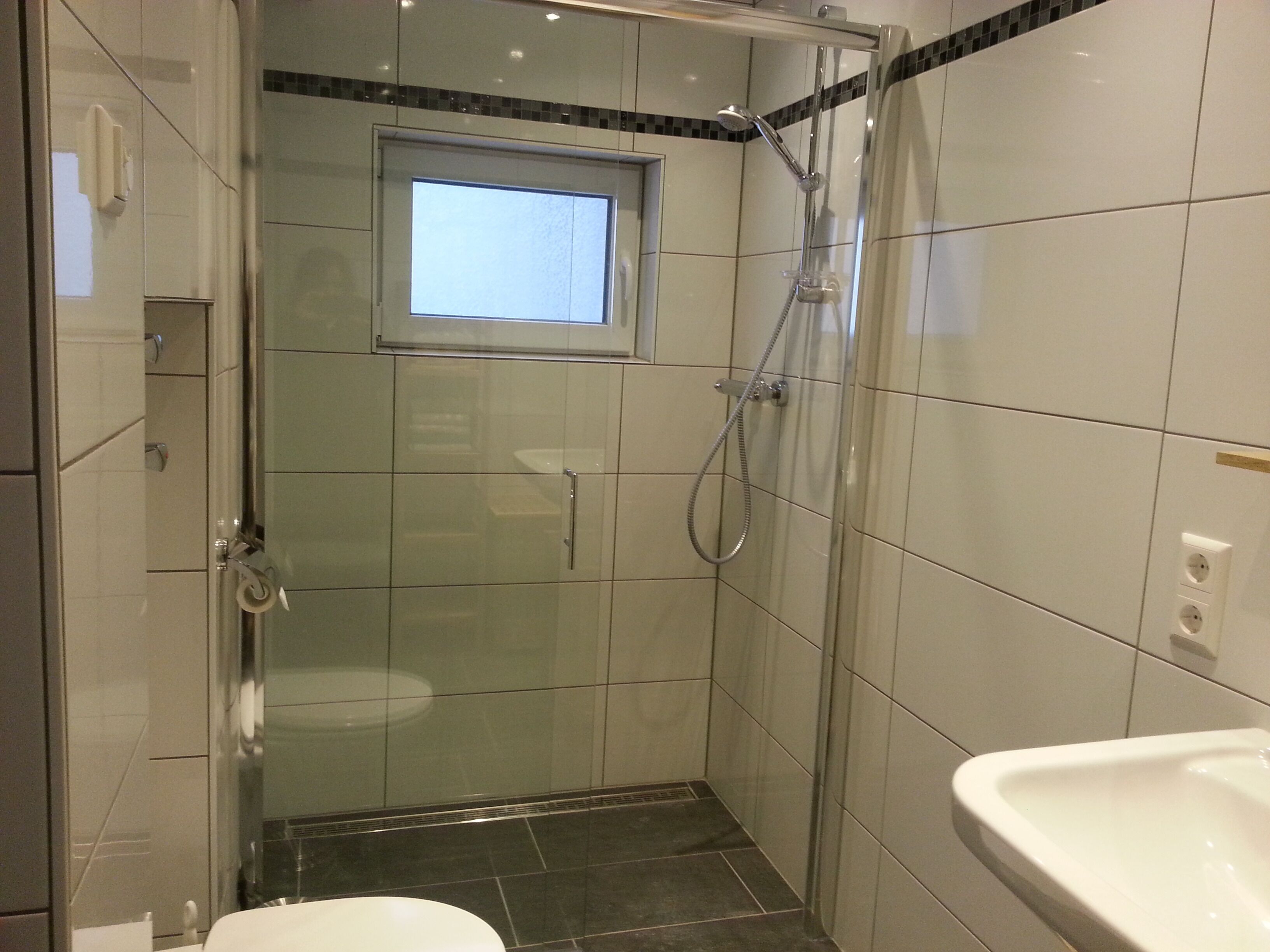 Un baño moderno con ducha de vidrio, una ventana sobre el inodoro y un lavamanos.