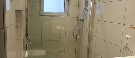 Un baño moderno con ducha de vidrio, una ventana sobre el inodoro y un lavamanos.